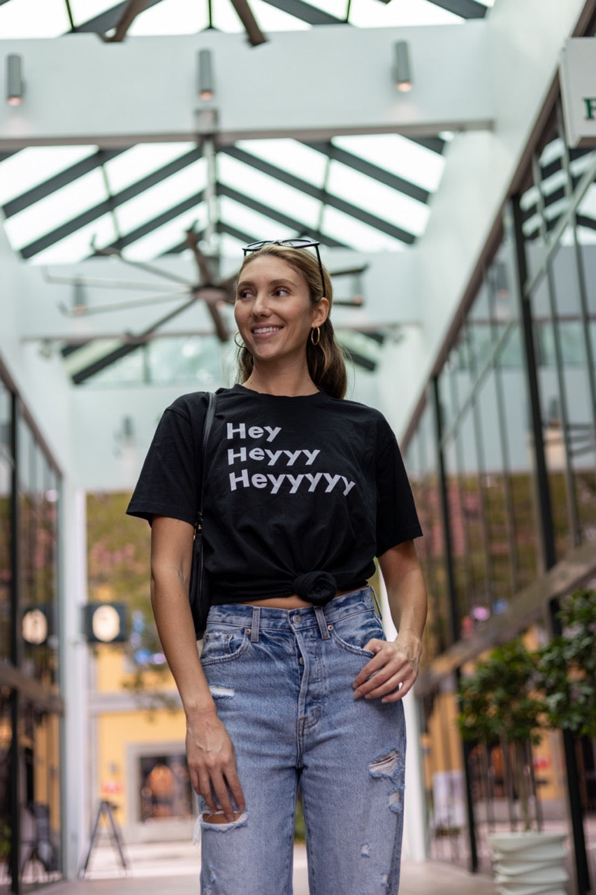 Hi Hey Heyyy Heyyyyy American Greeting T Shirt in black, Alia Buoniello models the Hi Hey Heyyy Heyyyyy Friendly Greet Tee by Happy interactions in Black at the Miami Design District