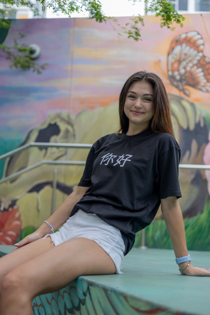 Dani Kott models the 你好 "Nĭhǎo" Hi in Chinese in Pinyin in black Greetings Tee Shirt from Happy interactions