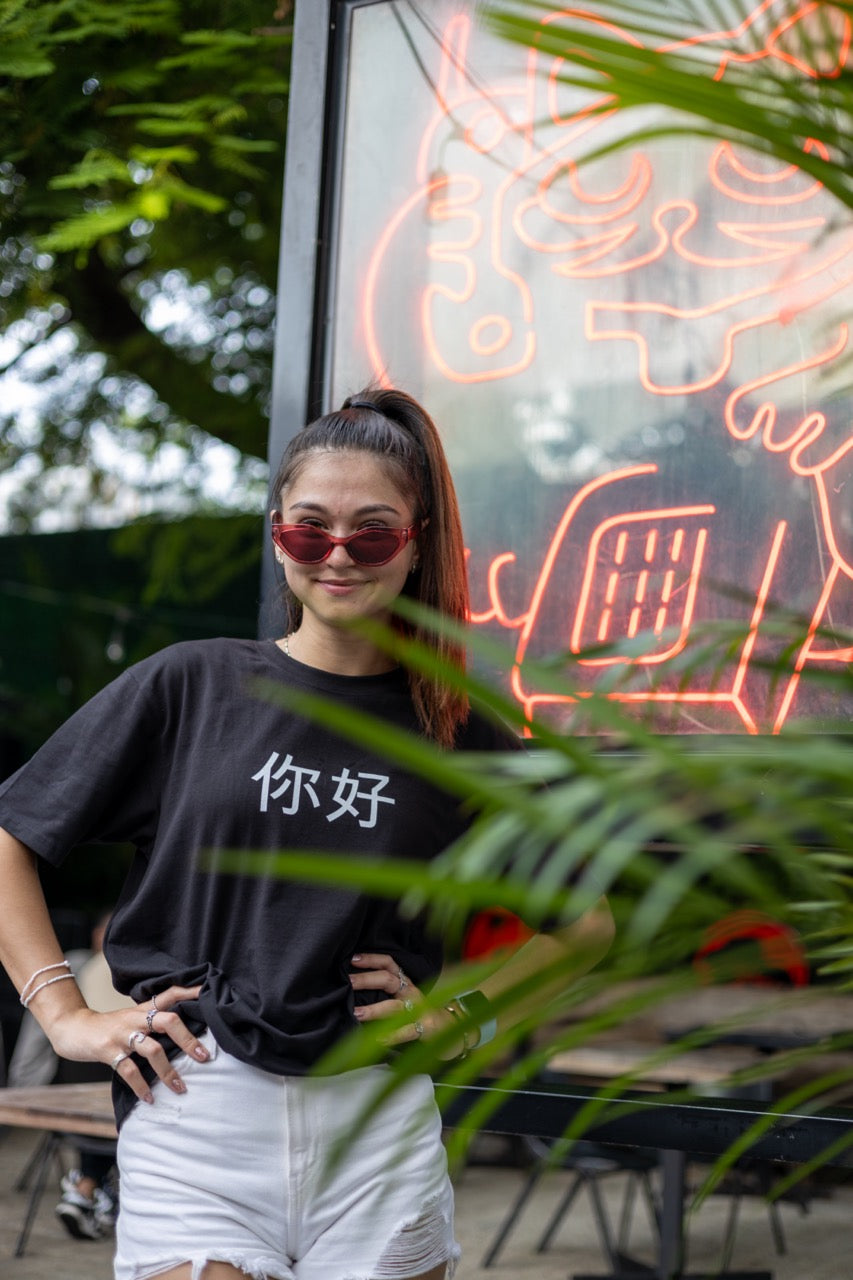 Dani Kott models the 你好 "Nĭhǎo" Hi in Chinese in Pinyin in black Greetings Tee Shirt from Happy interactions