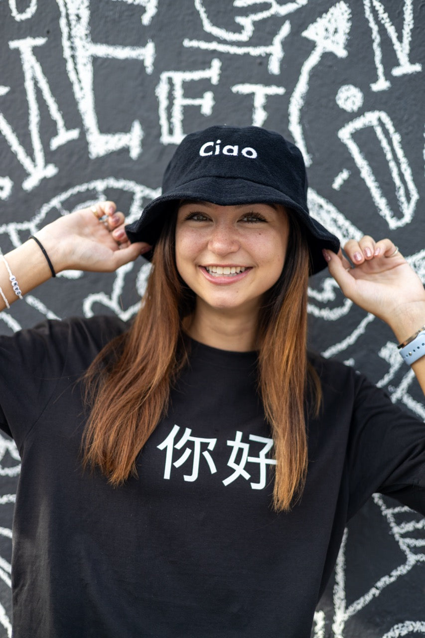 Dani Kott models the 你好 "Nĭhǎo" Hi in Chinese in Pinyin in black Greetings Tee Shirt and Ciao Fuzzy Bucket Hat from Happy interactions