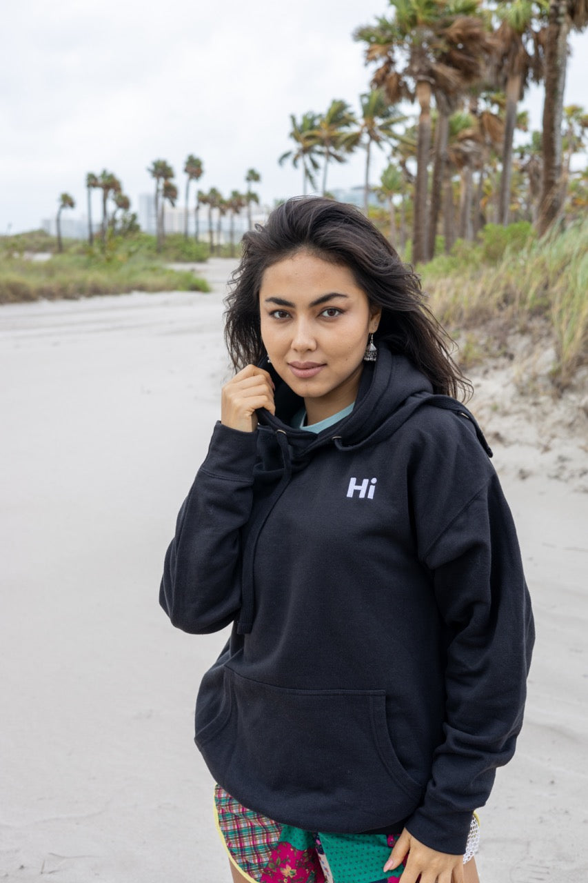 Hi lux embroidered Hoodie in black with Hi waving hand emoji on right sleeve, modeled by Assiya Mukanova