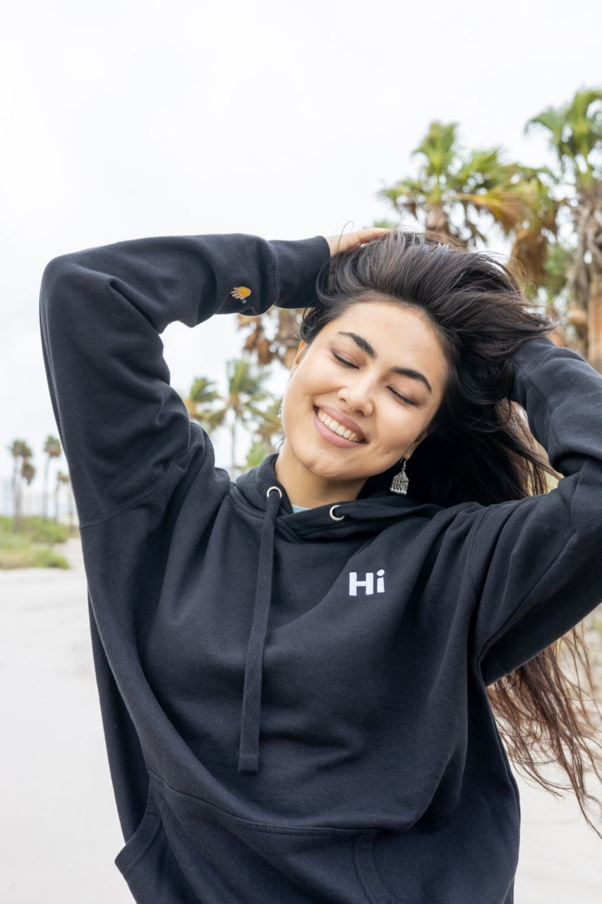 Hi lux embroidered Hoodie in black with Hi waving hand emoji on right sleeve, modeled by Assiya Mukanova