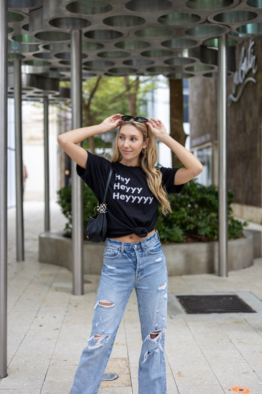 Hi Hey Heyyy Heyyyyy American Greeting T Shirt in black, Alia Buoniello models the Hi Hey Heyyy Heyyyyy Friendly Greet Tee by Happy interactions in Black at the Miami Design District