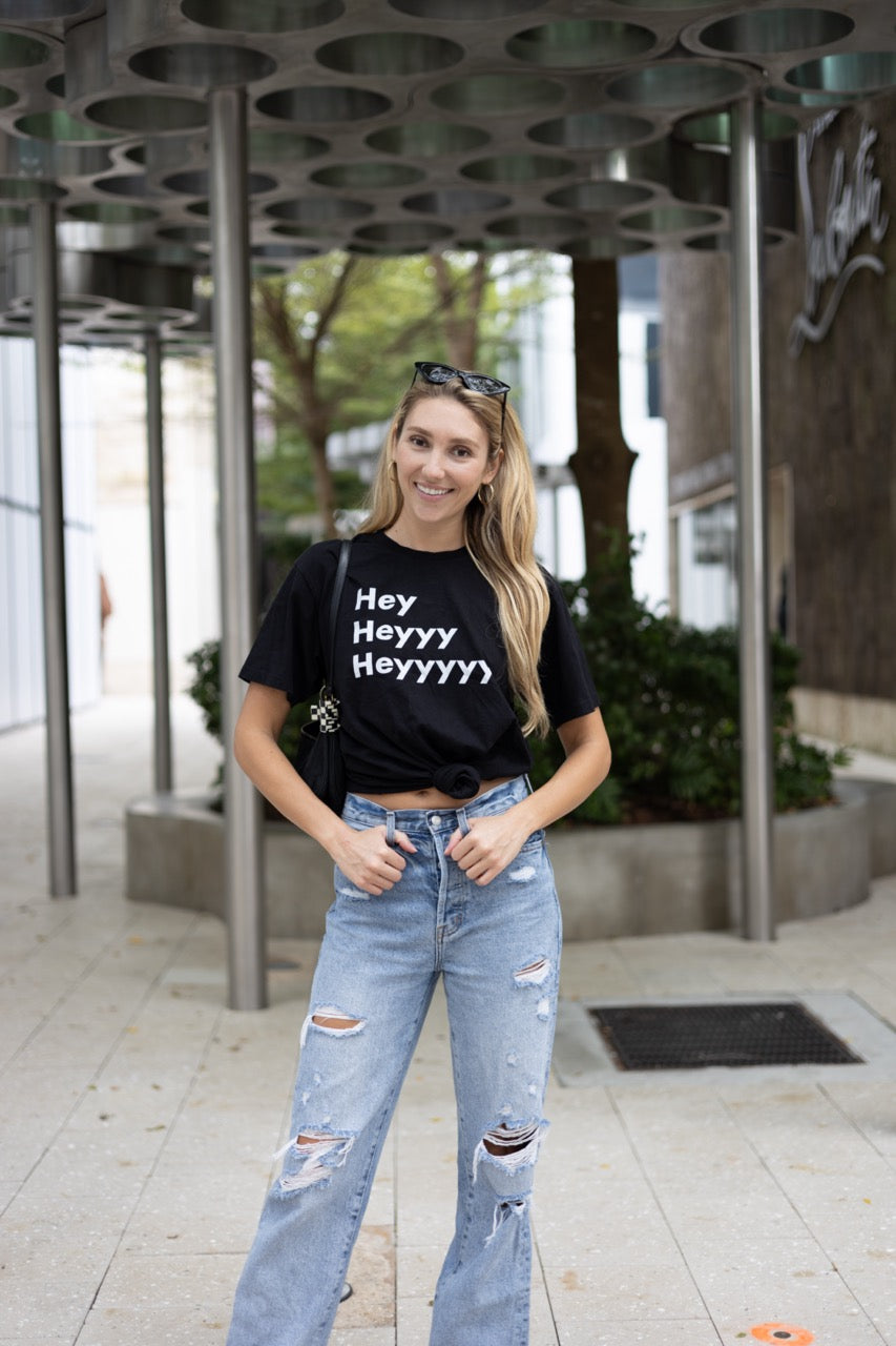 Hi Hey Heyyy Heyyyyy American Greeting T Shirt in black, Alia Buoniello models the Hi Hey Heyyy Heyyyyy Friendly Greet Tee by Happy interactions in Black at the Miami Design District