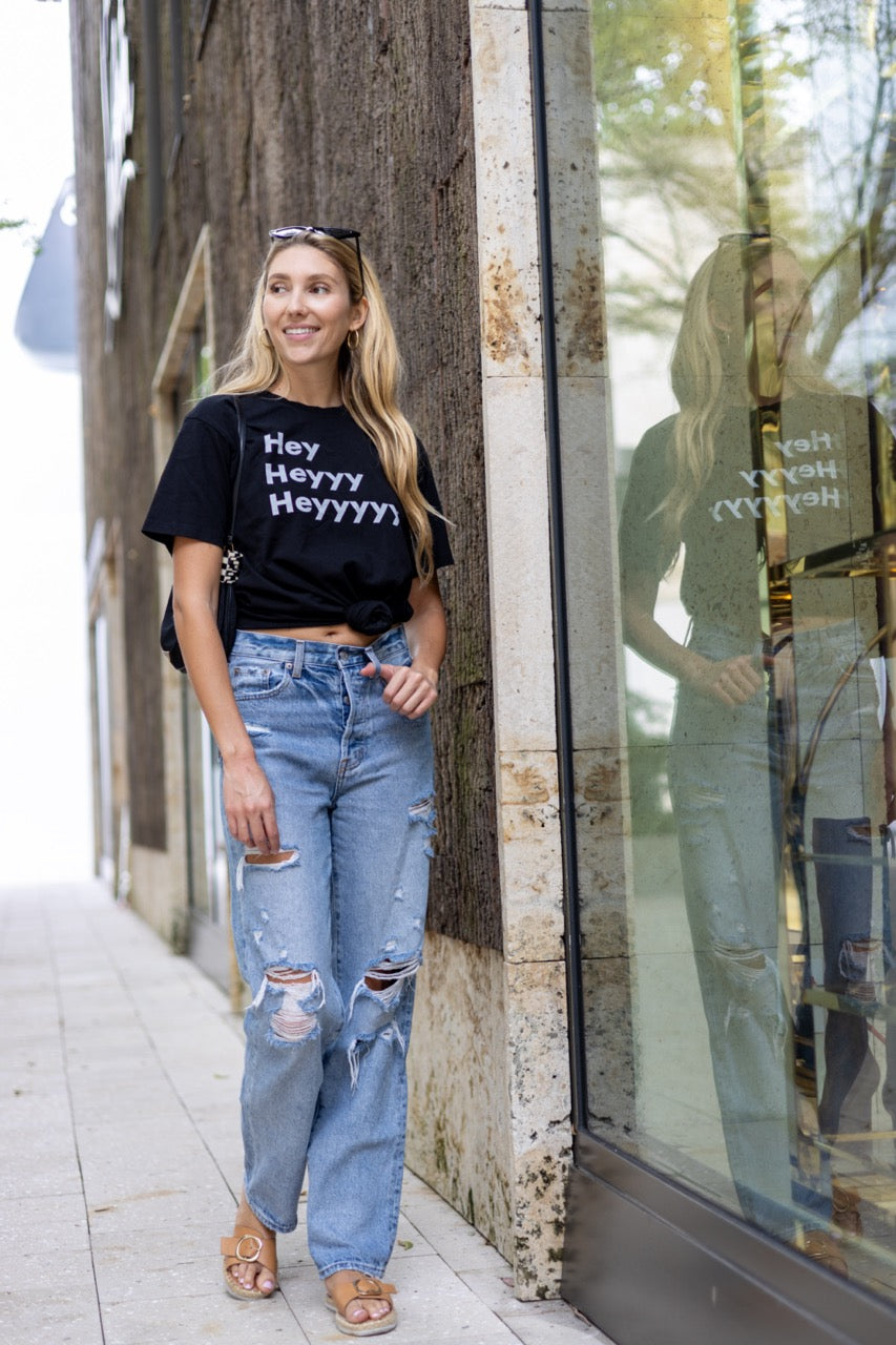 Hi Hey Heyyy Heyyyyy American Greeting T Shirt in black, Alia Buoniello models the Hi Hey Heyyy Heyyyyy Friendly Greet Tee by Happy interactions in Black at the Miami Design District