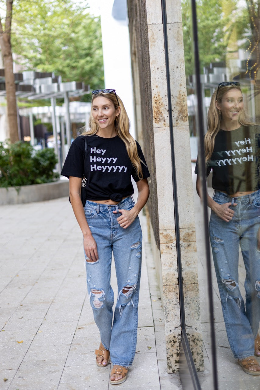 Hi Hey Heyyy Heyyyyy American Greeting T Shirt in black, Alia Buoniello models the Hi Hey Heyyy Heyyyyy Friendly Greet Tee by Happy interactions in Black at the Miami Design District