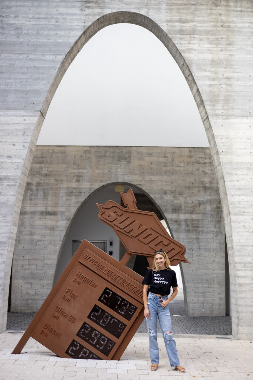 Hi Hey Heyyy Heyyyyy American Greeting T Shirt in black, Alia Buoniello models the Hi Hey Heyyy Heyyyyy Friendly Greet Tee by Happy interactions in Black at the Miami Design District near a Sunoco Gas Station piece of art