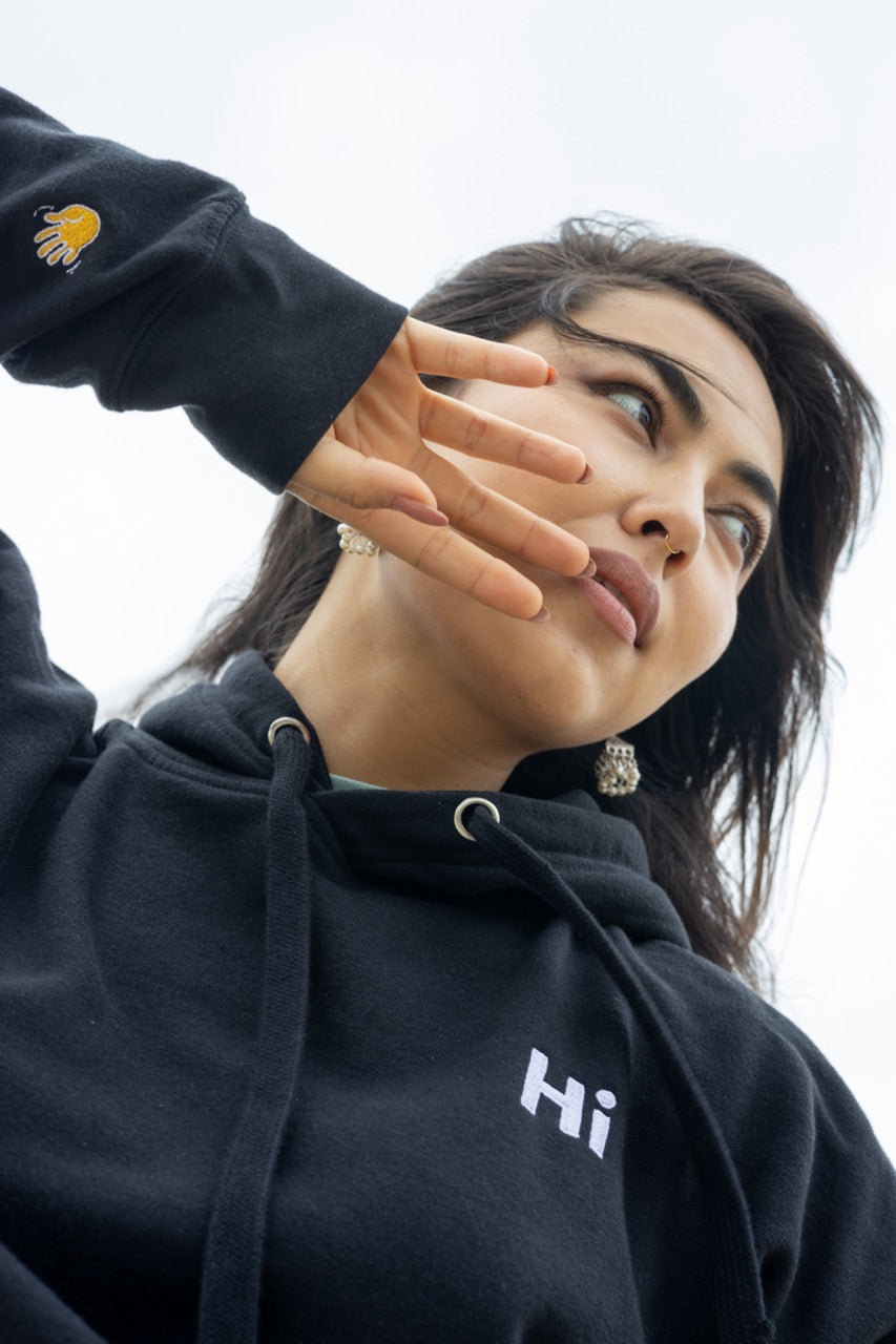 Hi lux embroidered Hoodie in black with Hi waving hand emoji on right sleeve, modeled by Assiya Mukanova