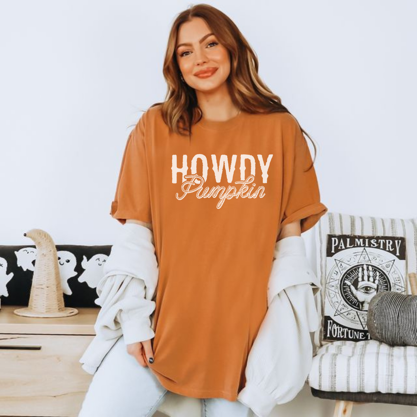Woman wearing a 'HOWDY Pumpkin' shirt in a cozy living room setting.