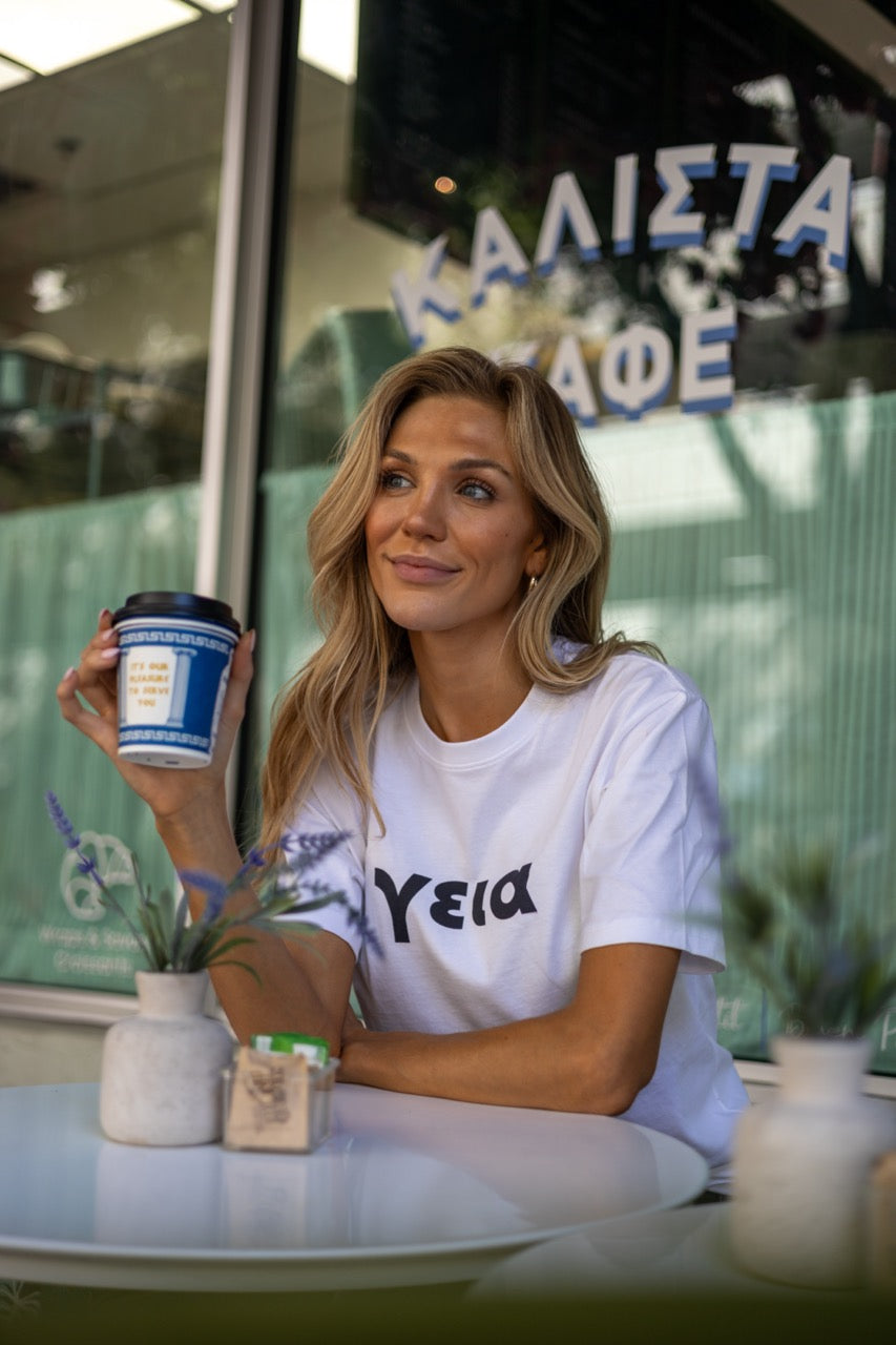 Hi γεια Greek Greet T shirt in white modeled by Victoria Peyton at Calista Cafe in Coconut Grove, Miami Florida, photography by Johnny Michael